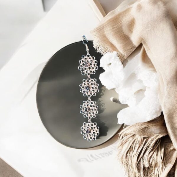 Pendientes largos de crochet Clara encima de un plato de cerámica, diseño floral único con destello de piedra de cristal