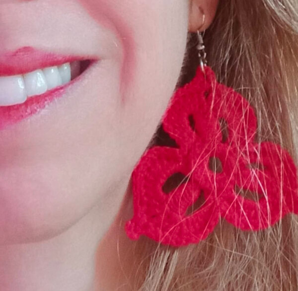 Pendientes Susi tejidos en hilo de perlé rojo mostrados en primer plano junto a sonrisa natural.