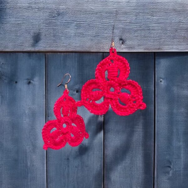 Aretes Susi en rojo vibrante exhibiendo su patrón de tres motivos sobre fondo de madera azul.