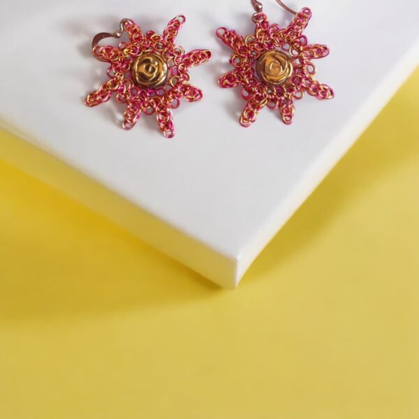 Pendientes cortos Alicia dorados con diseño artesanal en alambre y crochet,inspirados en la forma radiante de un sol, presentado sobre fondo amarillo.